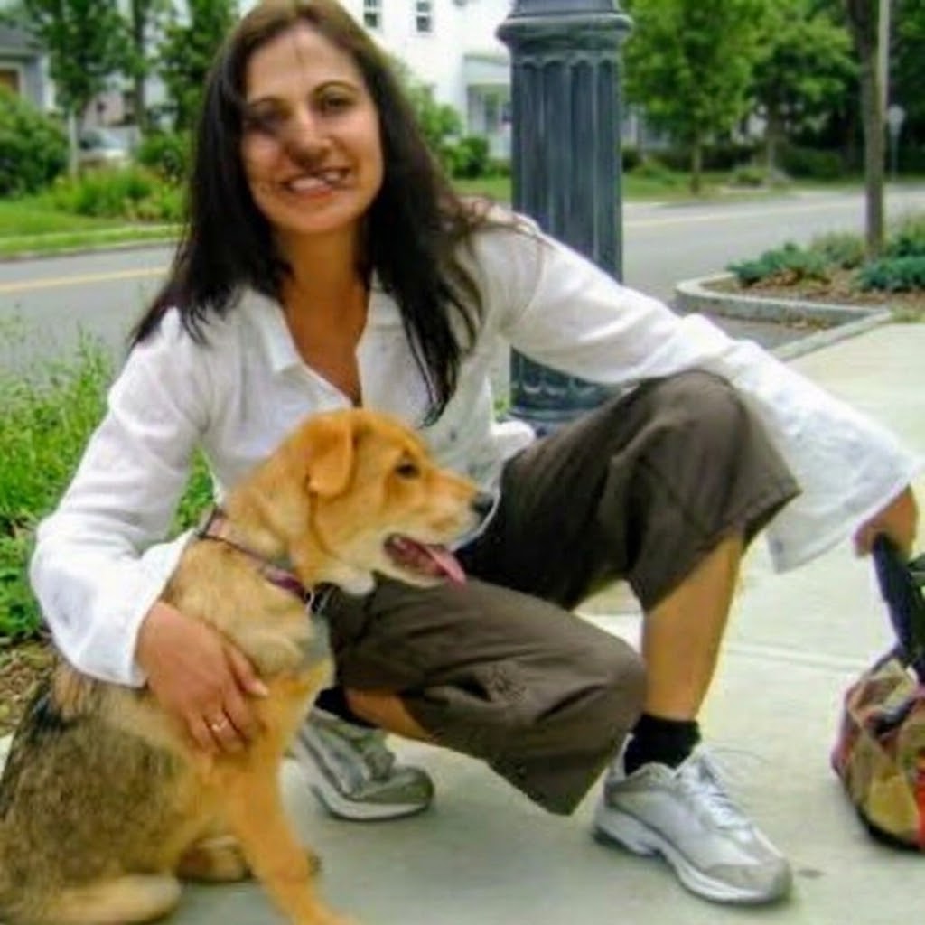 Neetu crouching on a tree-lined sidewalk, smiling, with a golden-brown dog beside her