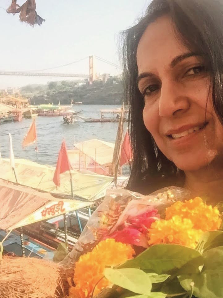 Neetu holding marigold flowers by a riverside during a spiritual practice