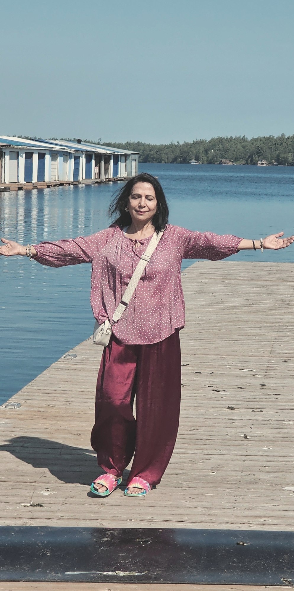 Neetu standing on a dock with arms open wide, eyes closed, in a moment of stillness by the water