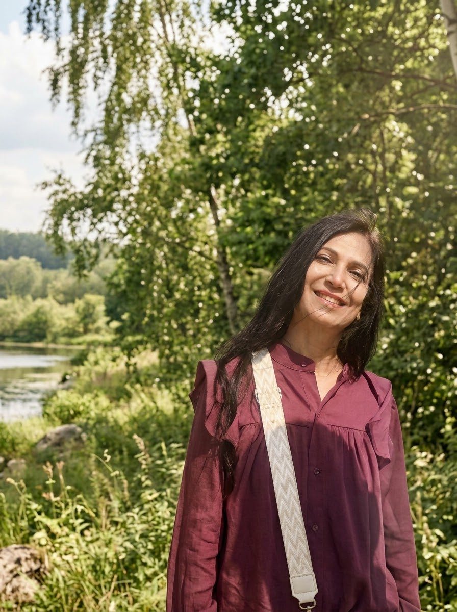 Neetu smiling warmly beside a river, surrounded by trees