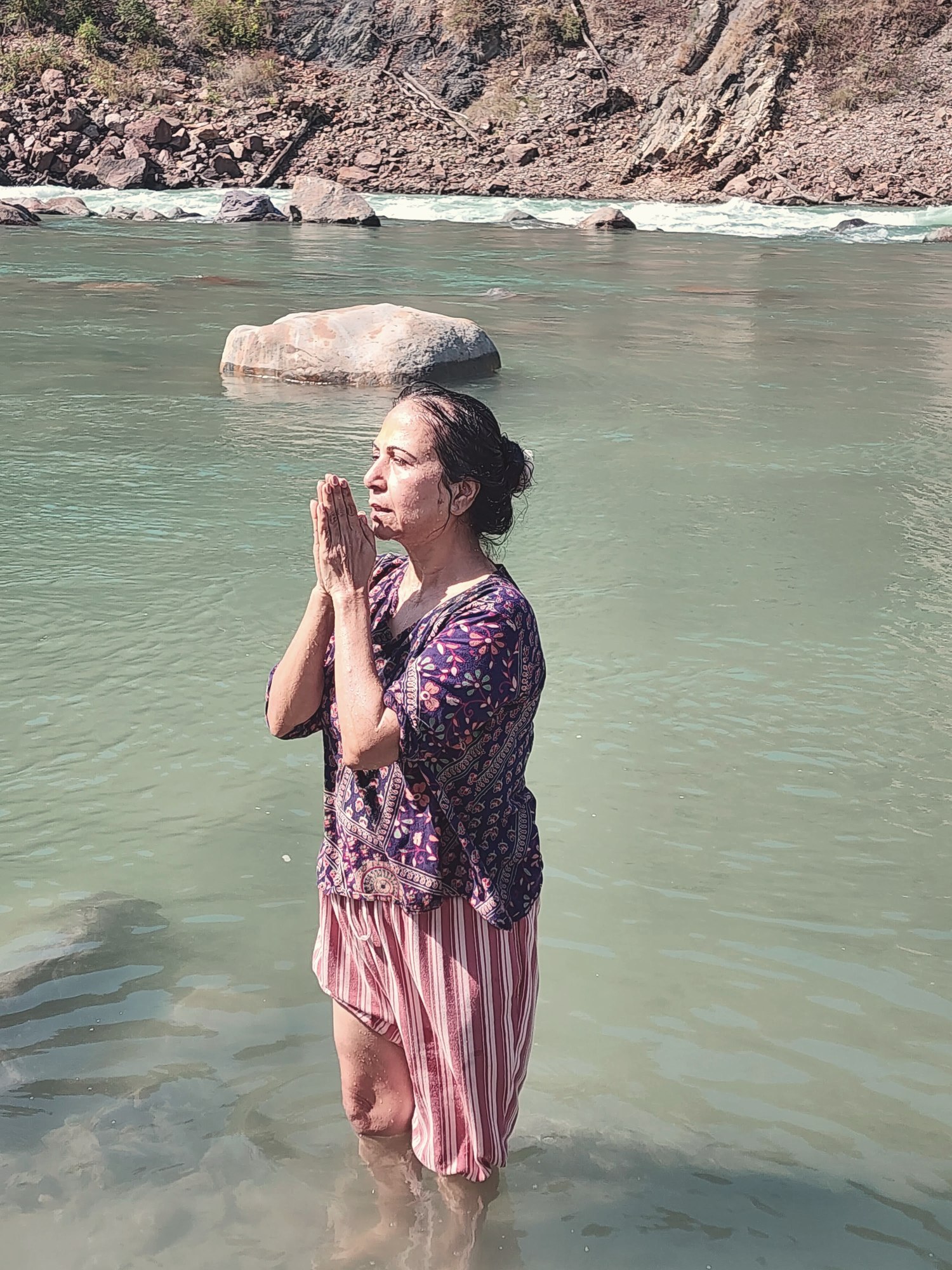 Neetu standing in flowing river water with hands together in a prayer position, symbolizing energy that travels